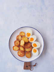 Crispy, browned baked potatoes and hard boiled egg halves on a white plate with blue border on blue background. Top view with copy space.