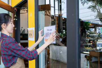 ฺBeautiful woman owner of small coffee shop puts up sign recruitment, need more employees after economic crisis.  restaurant entrepreneur concept. Happy female owner showing hiring sign in her shop.