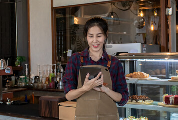 Happy Asian woman in apron standing taking order with tablet near bar counter coffee shop....