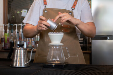 Professional barista wearing apron holding coffee grinder is being removed from coffee filter, come out pour coffee powder into drip machine, prepare dipping coffee for customers in cafe.