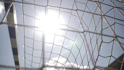 Low angle view of net. A slow motion shot of a football goal in sunlight.