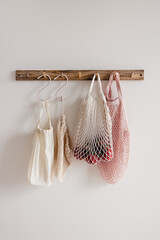 Wood hook rack with white and beige cotton mesh and canvas bag and red tomato on white wall on the modern style kitchen background. Smart organisation storage idea. Eco friendly grocery shopping.