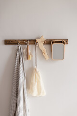 Wood hook rack with beige cotton mesh and canvas bag and wood treatment gua sha massage tool on white wall bathroom background. Smart organisation storage idea. Eco friendly skincare beauty routine.