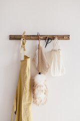 Wood hook rack with yellow linen apron, cotton mesh and canvas bag, pipidasta and scissors on white wall on the modern style kitchen background. Smart organisation storage idea. Eco friendly life.