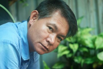 Obraz premium Close up beside veiw of a portrait of a middle-aged Asian man in a blue shirt, man alone concept.