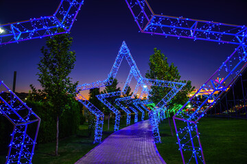 Decorations in the form of arches in the form of stars from LED lighting over the pavement in the night amusement park.