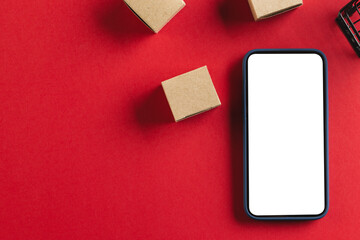 Smartphone with copy space and trolley with boxes on red background