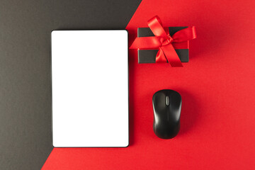 Tablet with blank screen, mouse and gift with copy space on red and black background