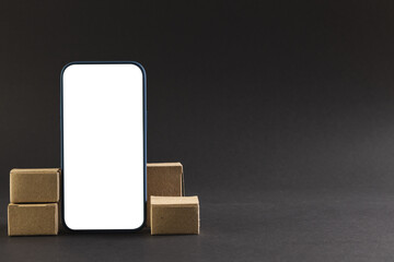 Smartphone with blank screen and cardboard boxes with copy space on black background