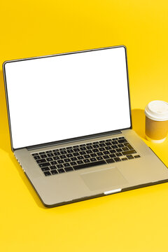 Vertical image of laptop with blank screen and takeaway cup with copy space on yellow background