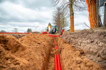 Network cables in red corrugated pipe are buried underground on the street. underground electric...