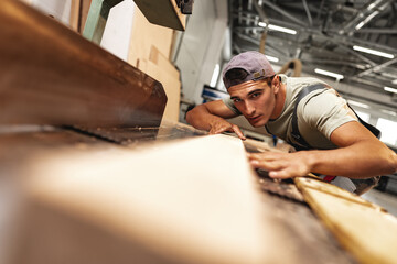 Young carpenter working on woodworking machines in the furniture factory
