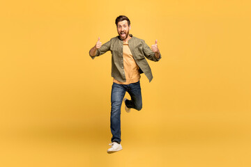 Fototapeta na wymiar Excited european middle aged man running towards camera, smiling and showing thumb up over yellow background