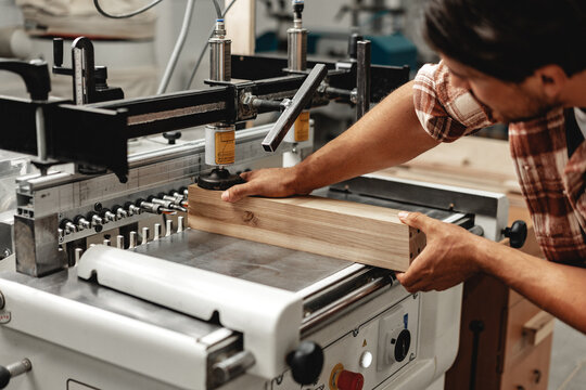 Young carpenter operating machine for wood processing at a furniture factory