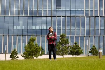 Fototapeta na wymiar A young woman with a laptop poses in an urban environment. African-American young woman in a red shirt and headphones.
