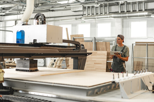 Young carpenter operating machine for wood processing at a furniture factory