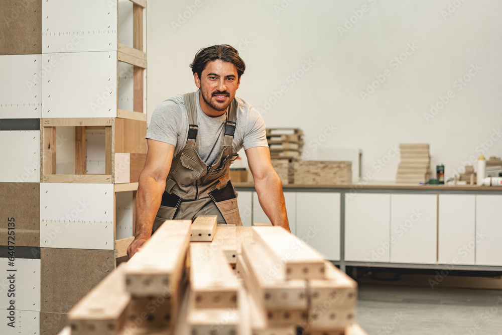 Wall mural young carpenter man looking and choosing wood plank at workshop in carpenter wood factory