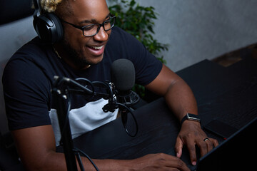 A black guy with glasses and headphones smiling in a home studio recording a podcast. Fashion...