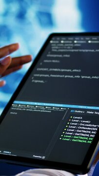 Vertical video Adept technician programming scripts on tablet, employing AI machine learning. Meticulous employee manipulating lines of code for artificial intelligence applications development, close