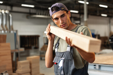 Young carpenter man looking and choosing wood plank at workshop in carpenter wood factory