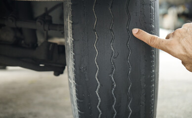 Close-up of man's hand pointing at old worn and bald tires from use. concept of tire wear and the...