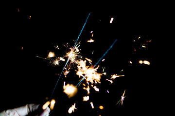 Hand holding a burning sparkler against fireworks background