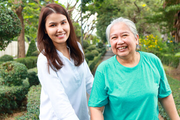 daughter or caregiver Take an elderly mother for a walk in an outdoor park, both smiling happily....