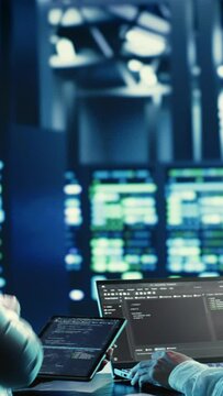 Vertical video Coworkers programming in server hub housing advanced infrastructure storing massive datasets. Employees running code on laptop to update data center racks doing complex computational