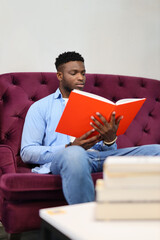 A young man engrossed in reading books at home, embracing a leisurely educational moment.