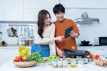 Happy Family portrait of loving young asian of having fun standing a cheerful preparing food See in the tablet and enjoy cook cooking meat, bread while standing on a kitchen Condo life or home