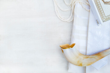A shofar is placed on a tallit and siddur book on a white background. photographed from above.   A symbol of the Rosh Hashanah holiday. Suitable for shana tova greeting card and Yom Kippur. with free  © Talcoco photoart