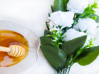 A bowl of honey with a pouring stick and a bouquet of white flowers on a white background with a wood texture. A symbol of the Rosh Hashanah holiday. Suitable for shana tova greeting card 