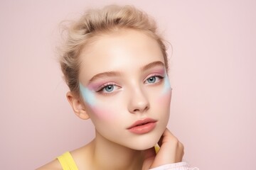 Portrait of a teenage girl with light art makeup on pastel pink background, close-up.