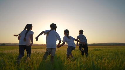Fototapeta na wymiar a group of children run across the field on the grass. happy family kid dream concept. children running in a field lifestyle with tall grass. girls holding hands in the foreground on the sunset