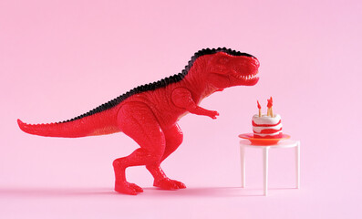 Cute dinosaur toy with birthday cake on table on pink background