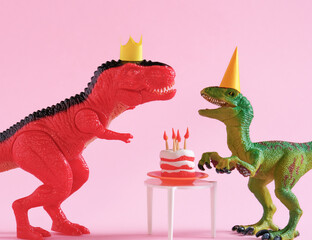 Cute happy green and red dinosaurs in birthday hats with cake with flaming candles on pastel pink background. Copy space. Minimal art birthday card idea.