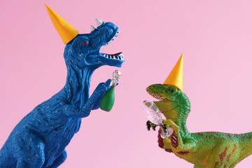 Toy dinosaurs with champagne and glass on pink background.