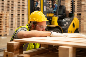 A guy carpenter in a hardhat and glasses inspects a completed work item at a timber industry.