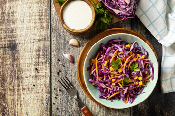 Homemade purple cabbage salad with corn, carrots and greek yogurt on a rustic table. Vegan food concept, healthy food. View from above. Copy space.
