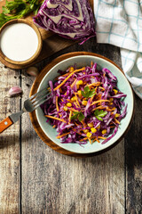 Vegan food concept, healthy food. Homemade purple cabbage salad with corn, carrots and greek yogurt on a rustic table. View from above. Copy space.