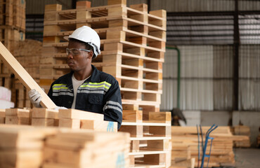 Female carpenter working in a woodworking factory, He is wearing a safety helmet and glasses.Checking the wooden planks coming out of the wood grinder.