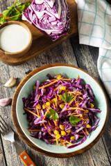 Vegan food concept, healthy food. Homemade purple cabbage salad with corn, carrots and Greek yogurt on a rustic table.