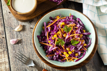Homemade purple cabbage salad with corn, carrots and greek yogurt on a rustic table. Vegan food concept, healthy food.
