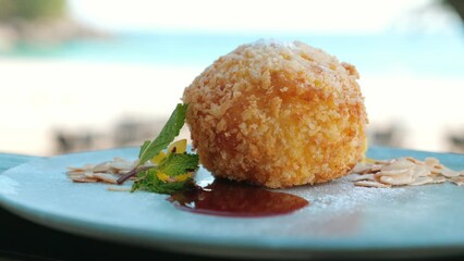 Stuffed fried ice cream with strawberry sauce and mint leaf on white plate. Gourmet dessert served at a tropical restaurant. Concept of a delightful treat for a holiday meal.