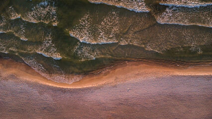 Sea waves at sunset on the Baltic Sea. A sandy beach in Kolobřeh. Taken from a drone. Kołobrzeg is city in Poland. Top down - obrazy, fototapety, plakaty