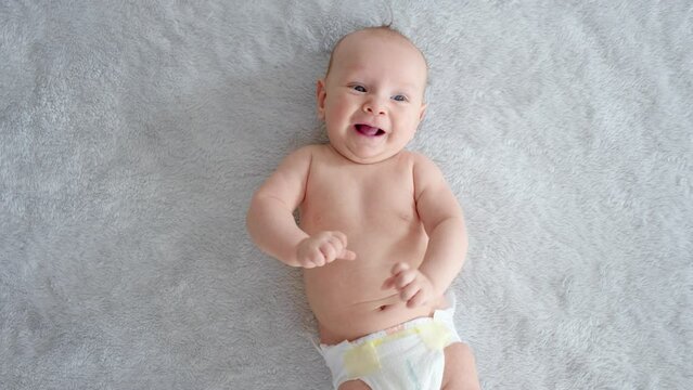 Happy newborn boy lies on a blue blanket and actively moves his arms and legs.  A healthy newborn baby in a nappy without clothes.    Cute baby with blue eyes . Slow motion. Half Full  length body.