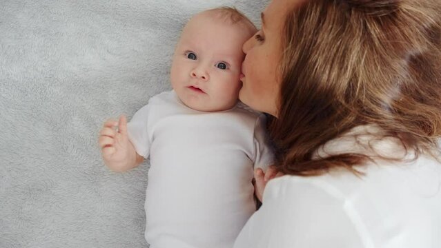 Happy newborn baby with his mother. Closeup Faces of the mother and infant baby. Healthy newborn baby in a white t-shirt with mom.  Cute Infant boy and parent, top view. Slow motion. Happy family