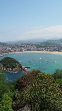 Aerial view of La Concha bay in San Sebastian city during summer with boats on the shore and the beach. Vertical panoramic video with copy space of beach city with turquoise water.