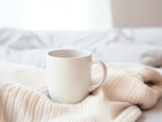Blank empty white coffee mug mockup on warm knitted clothes in autumn and winter season