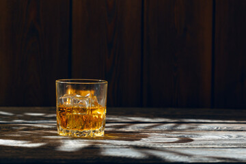 A glass of whiskey and ice stands on an old wooden table